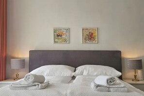 A neatly made bed with white linens and two pillows, a dark headboard, and two framed abstract paintings on the wall. - Red Orange Palm - 200m2 - stylish, original, central  (Vienna)
