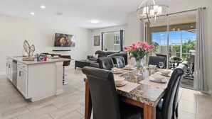 Una cocina moderna con una isla central, comedor con mesa de mármol y sala de estar con sofá y ventana grande.