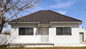 Une maison de plain-pied avec un toit sombre, un revêtement extérieur blanc et une clôture en bois peinte en blanc.