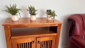 Une console en bois surmontée de trois plantes en pot, une chaise en cuir à droite et un plancher en bois.