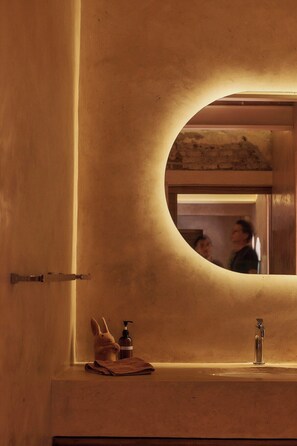 Bathroom features an oval mirror embedded in a textured wall and offers a sink with basic amenities.