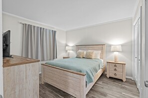 A bedroom with a wooden bed, bedside tables, a TV, and curtains.