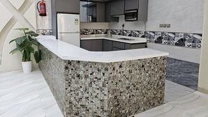 Uma cozinha moderna com bancada de mármore, micro-ondas embutido e frigorífico.