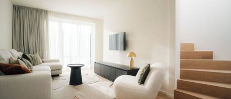 A modern living room with a sofa, a coffee table, a lamp, and a TV on the wall.