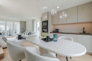 A modern kitchen with a dining area, large windows, and a view of the city. - Apartments Hotel Stadt Hamburg (Sylt)