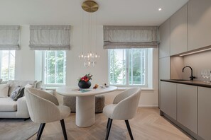 A modern kitchen with a round dining table, two chairs, a chandelier, and a built-in oven. - Apartments Hotel Stadt Hamburg (Sylt)