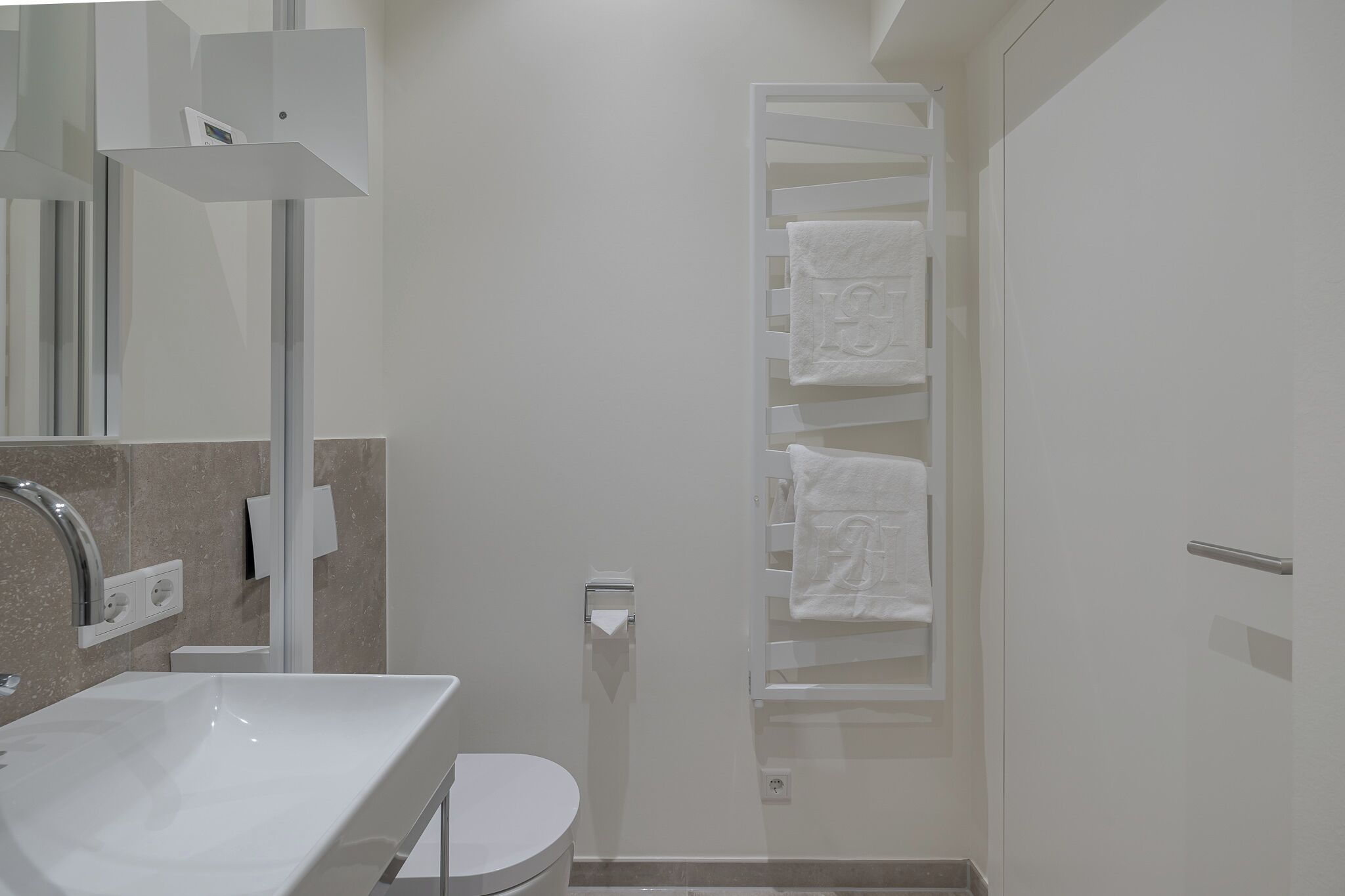 A modern bathroom with a white sink, toilet, and towel rack.