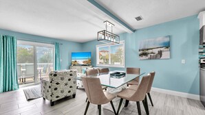 A modern living room with a glass dining table, comfortable seating, a TV, and a balcony with a view. - ☀️30A Steps to Beach in 30A-Bikes-Blue Dolphin (Santa Rosa Beach)