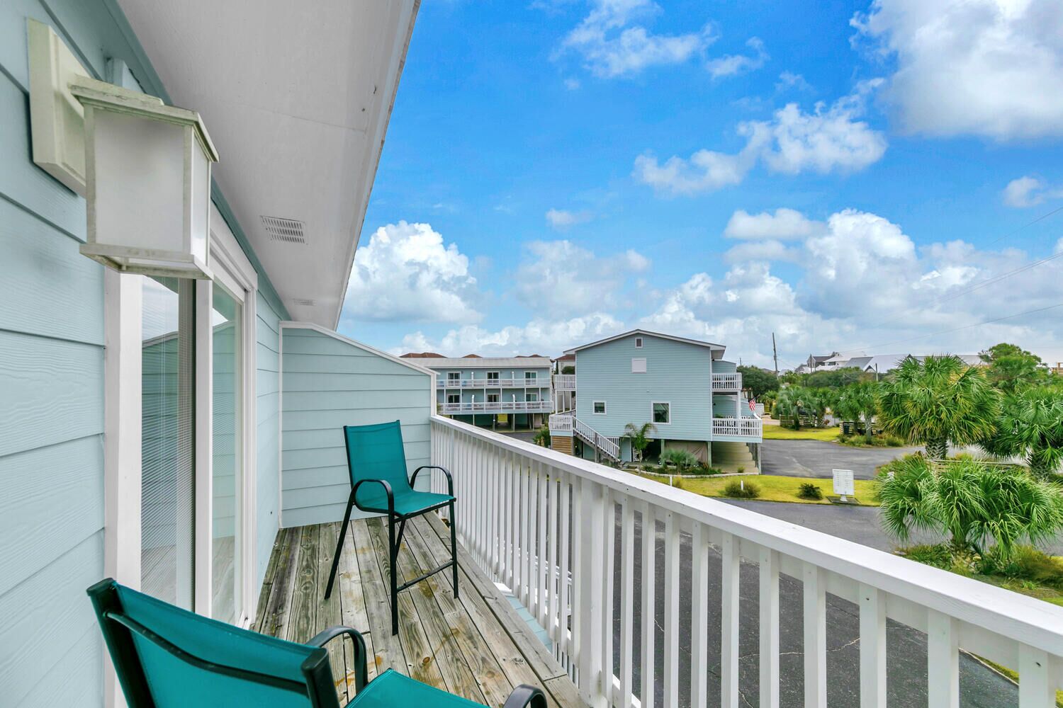 A balcony with two green chairs, a white railing, and a view of a building complex with multiple units.