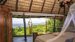 A room with a bed, a view of the ocean, a hammock, and a thatched roof. - Casa El Paraíso (Las Galeras)