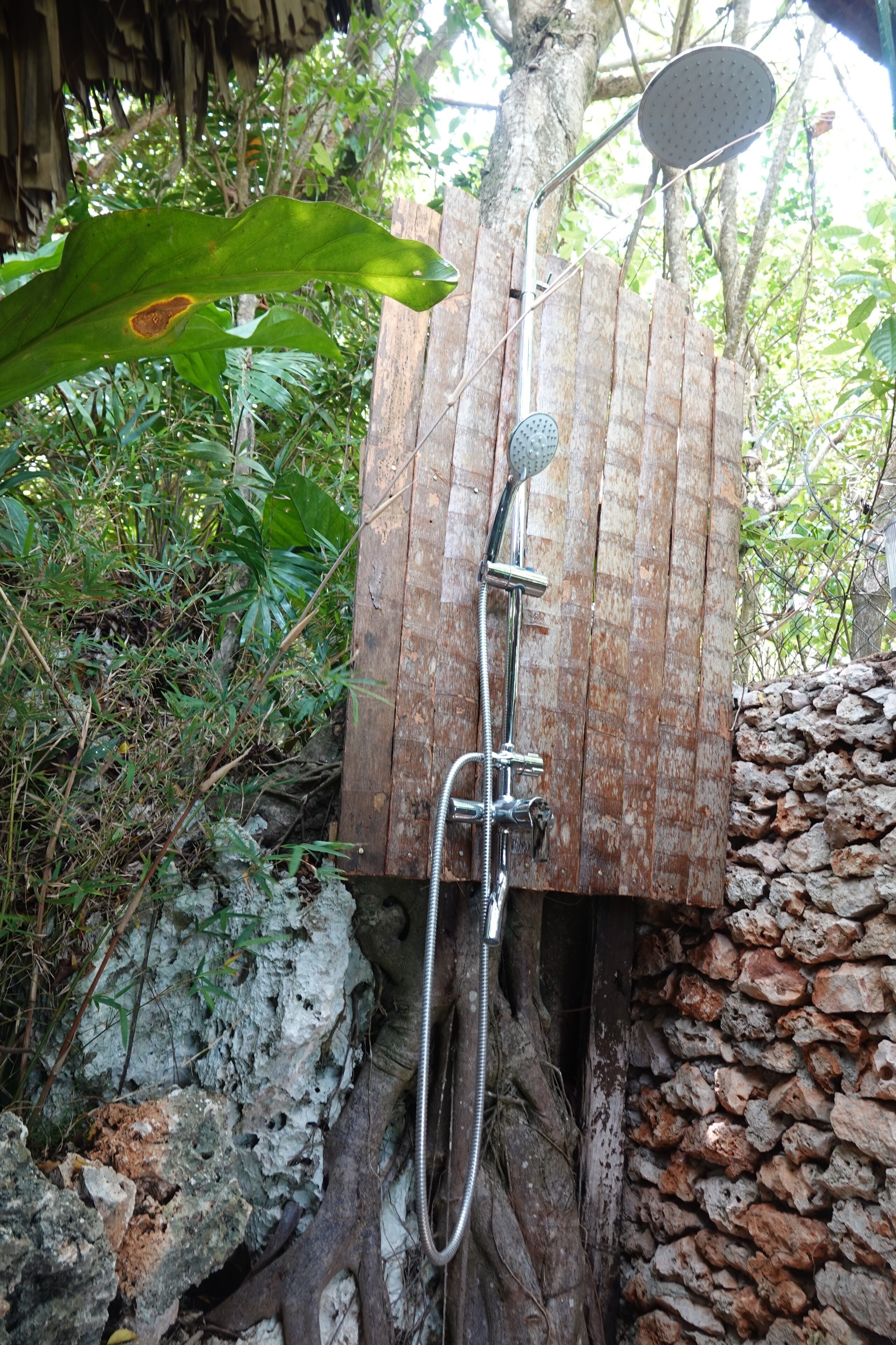 Un cabezal de ducha fijado a una estructura de madera con un muro de piedra.