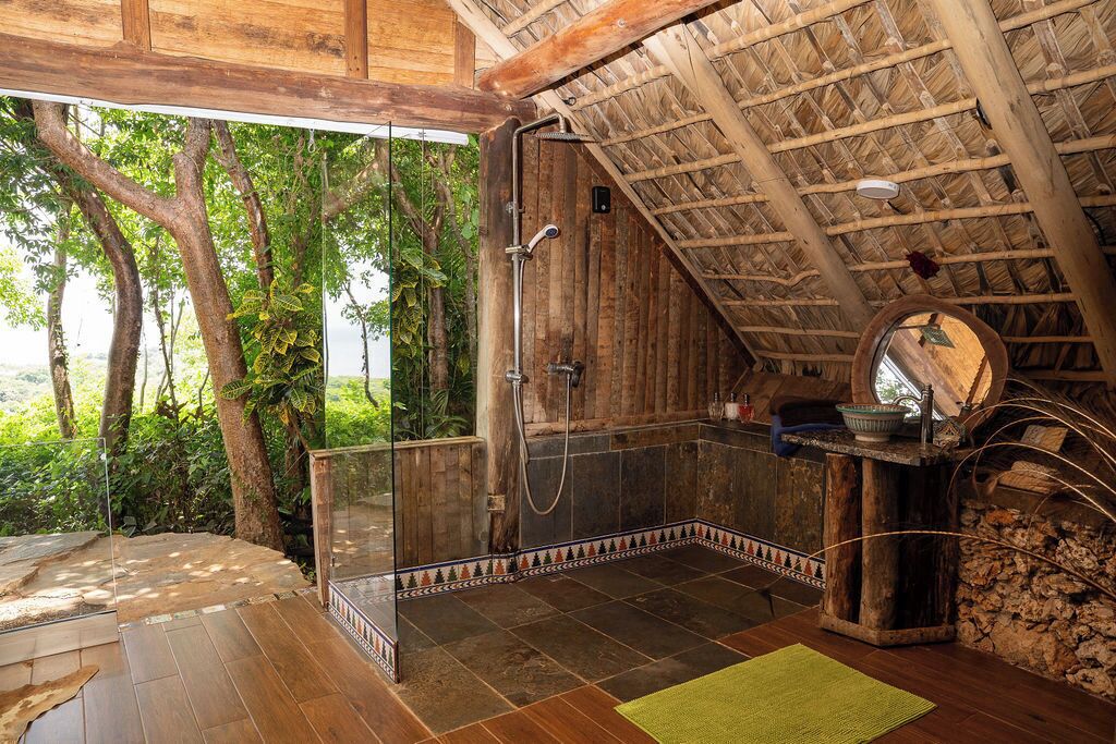 Un bagno in legno con box doccia in vetro, pavimento in pietra e tetto in paglia.
