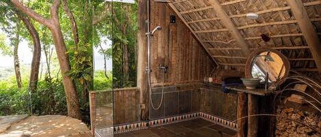 Un bagno in legno con box doccia in vetro, pavimento in pietra e tetto in paglia.