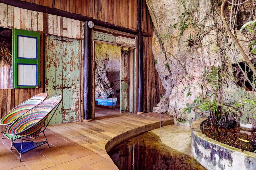 A rustic interior with a wooden floor, a colorful chair, a small water feature, and a door leading to another room.