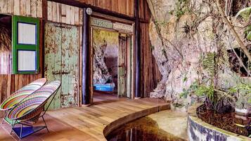 A rustic interior with a wooden floor, a colorful chair, a small water feature, and a door leading to another room.