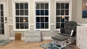 A room with large windows, a rocking chair, wicker baskets, and a wooden floor.