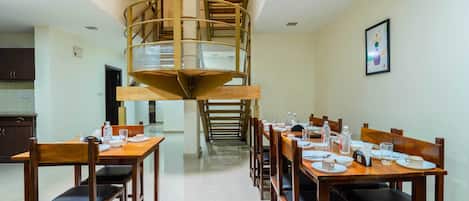 A dining area with a spiral staircase leading to an upper level, wooden tables and chairs, and a kitchen visible in the background.