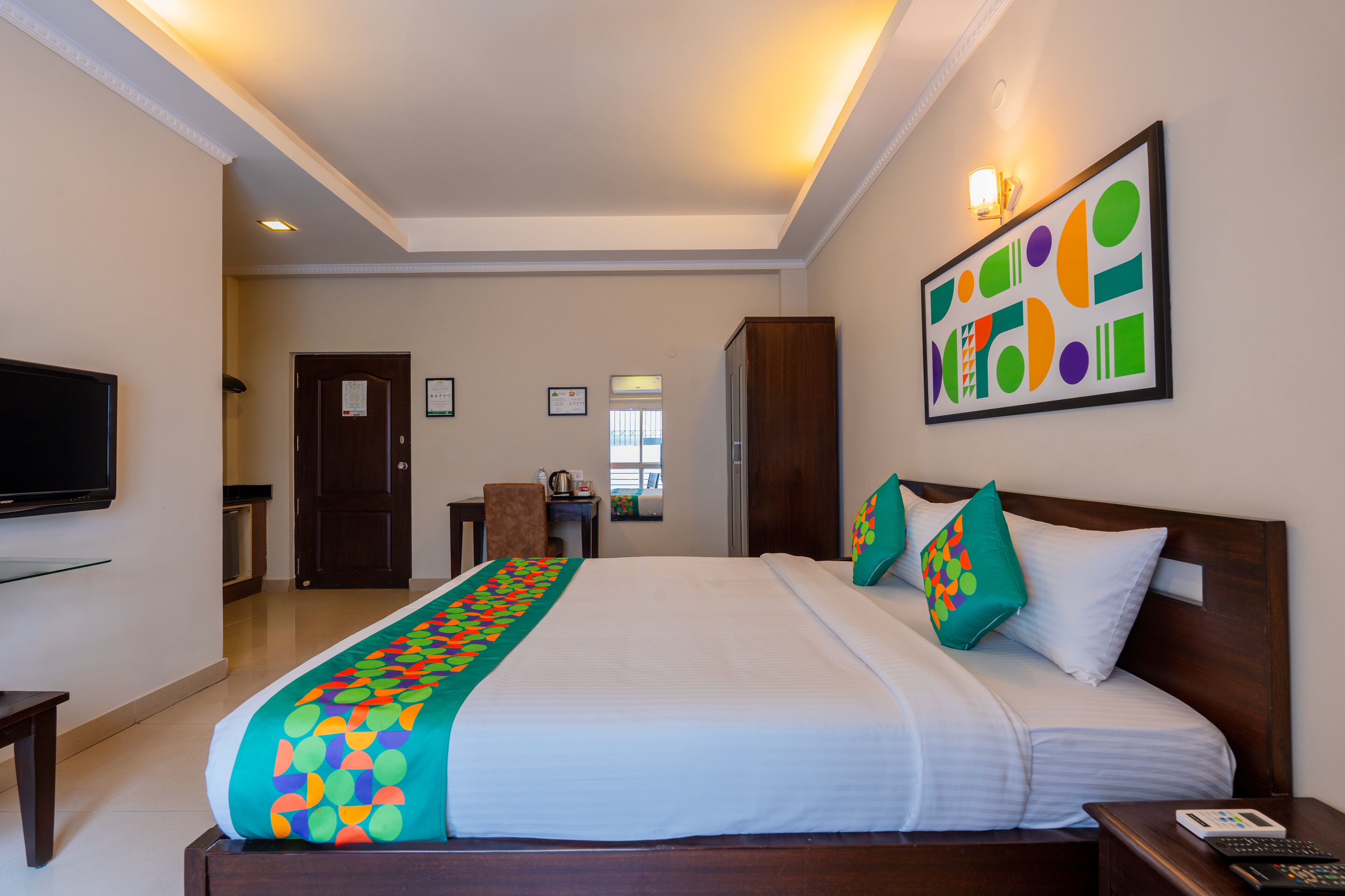 Une chambre d’hôtel avec un grand lit, une télévision, un bureau et une œuvre d’art accrochée au mur.