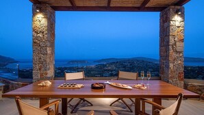 A dining table set for two with stone pillars, overlooking a scenic view of a coastal landscape.