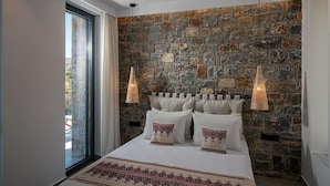 A bedroom with a stone wall, a large bed with white bedding, and two pendant lights.