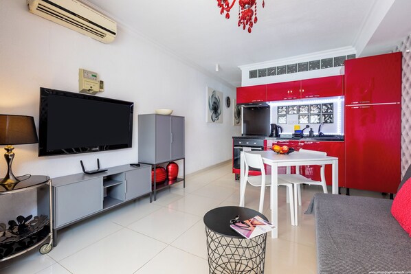 Una cocina moderna con armarios rojos, un televisor de pantalla plana y un comedor con mesa y sillas.