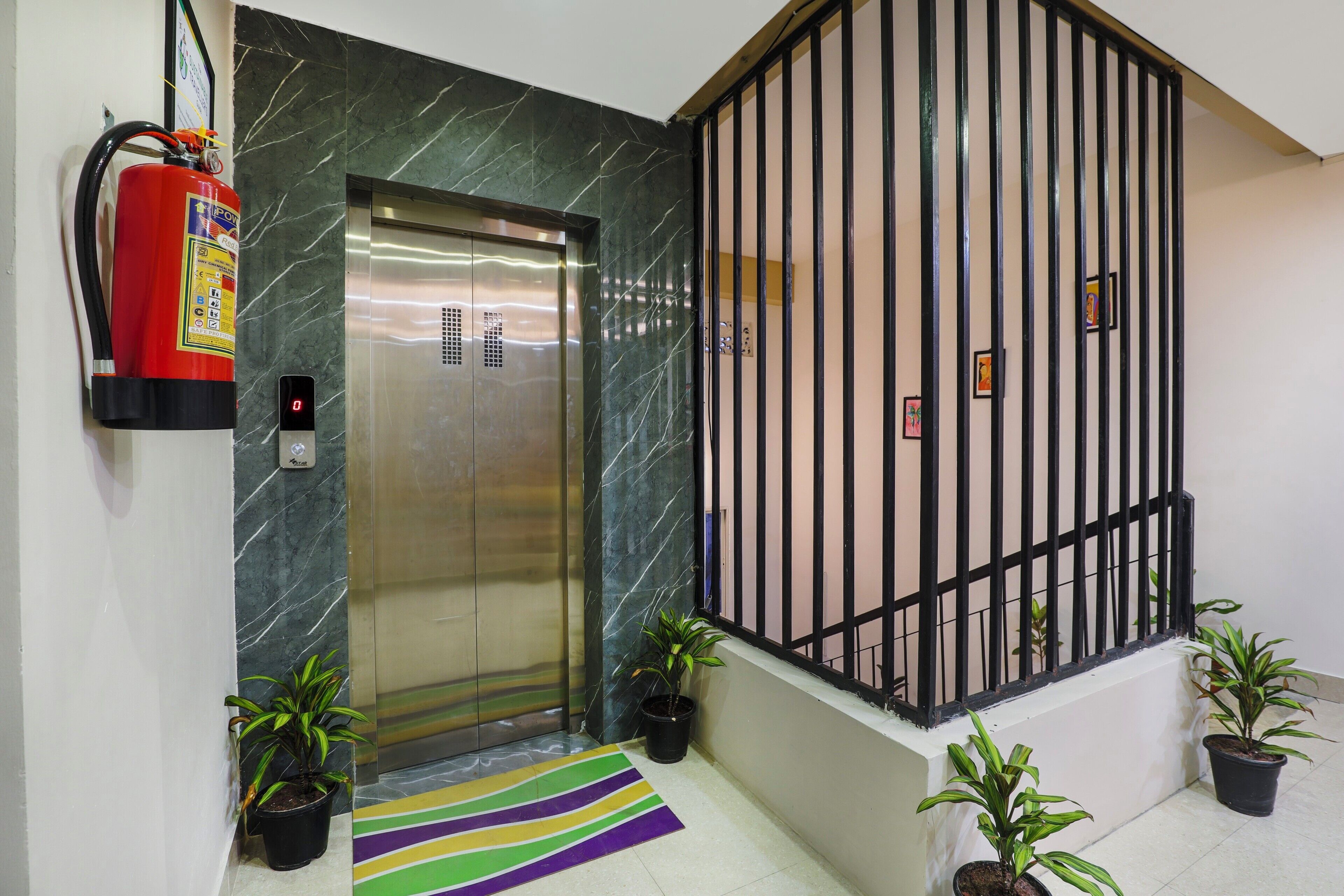 An elevator, a fire extinguisher, a staircase with a metal railing, and potted plants.