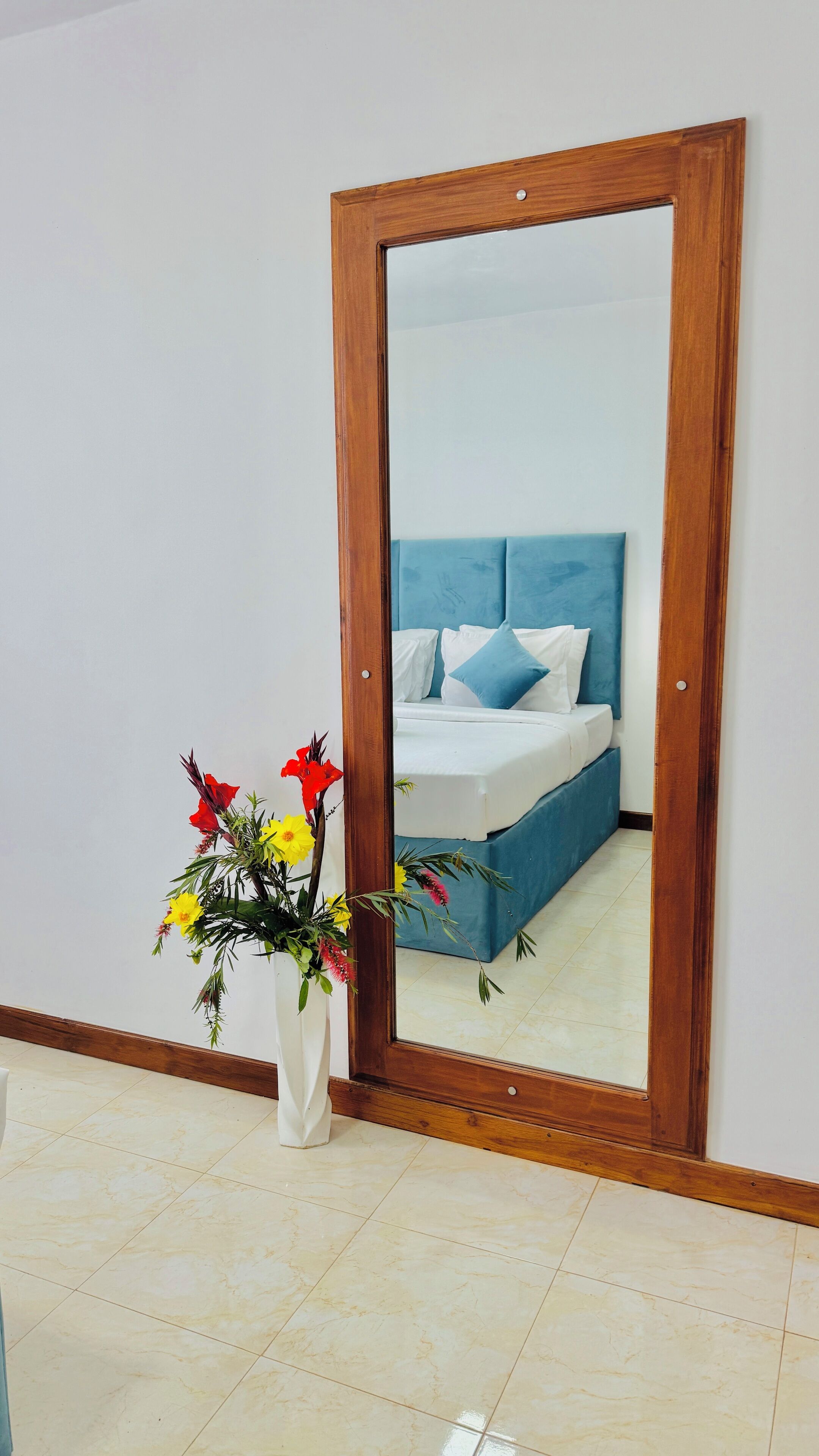 A bedroom with a bed, a blue headboard, and a mirror with a wooden frame.