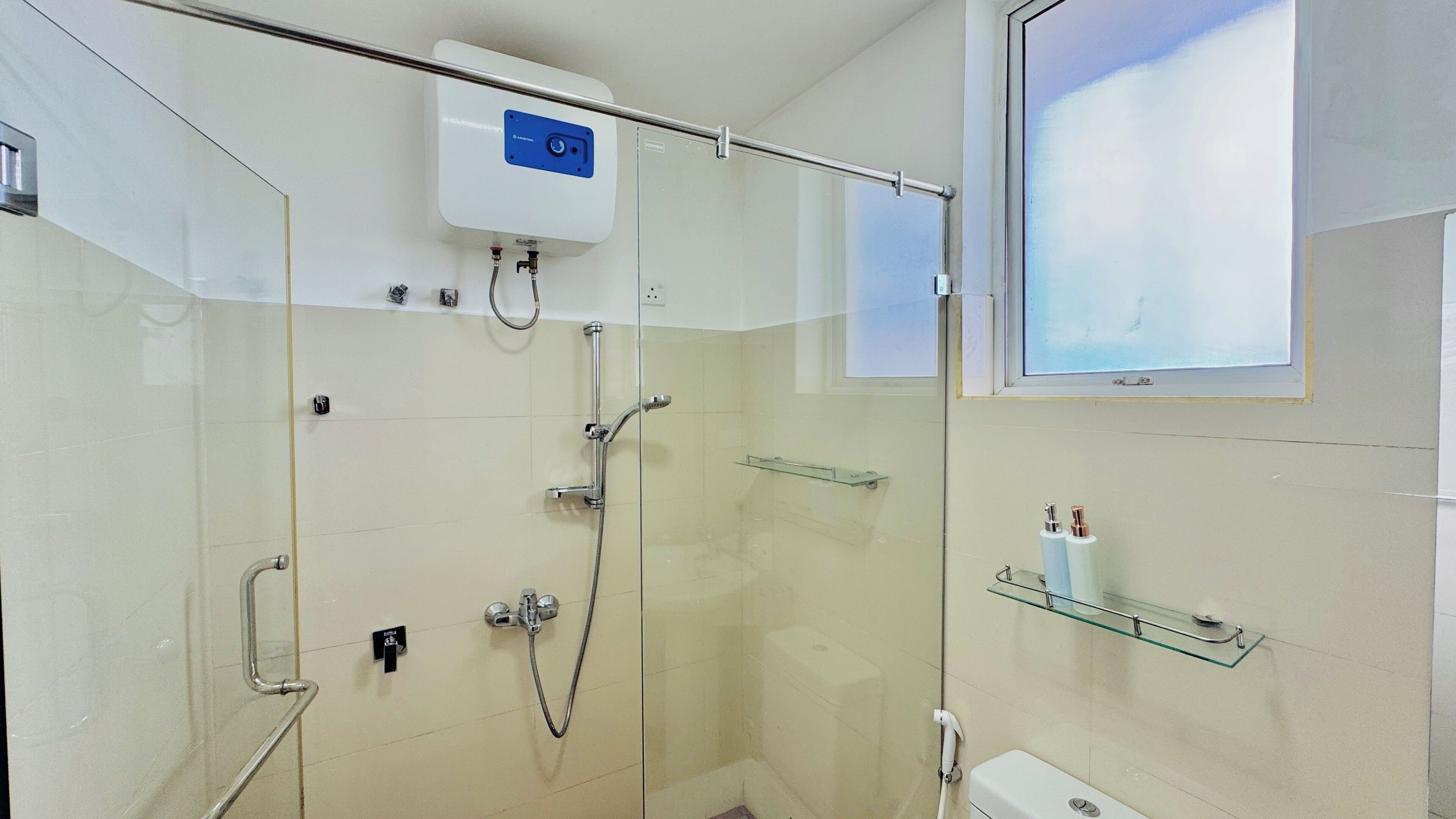 Un baño moderno con cabina de ducha de vidrio, inodoro y repisa de vidrio con artículos de tocador.
