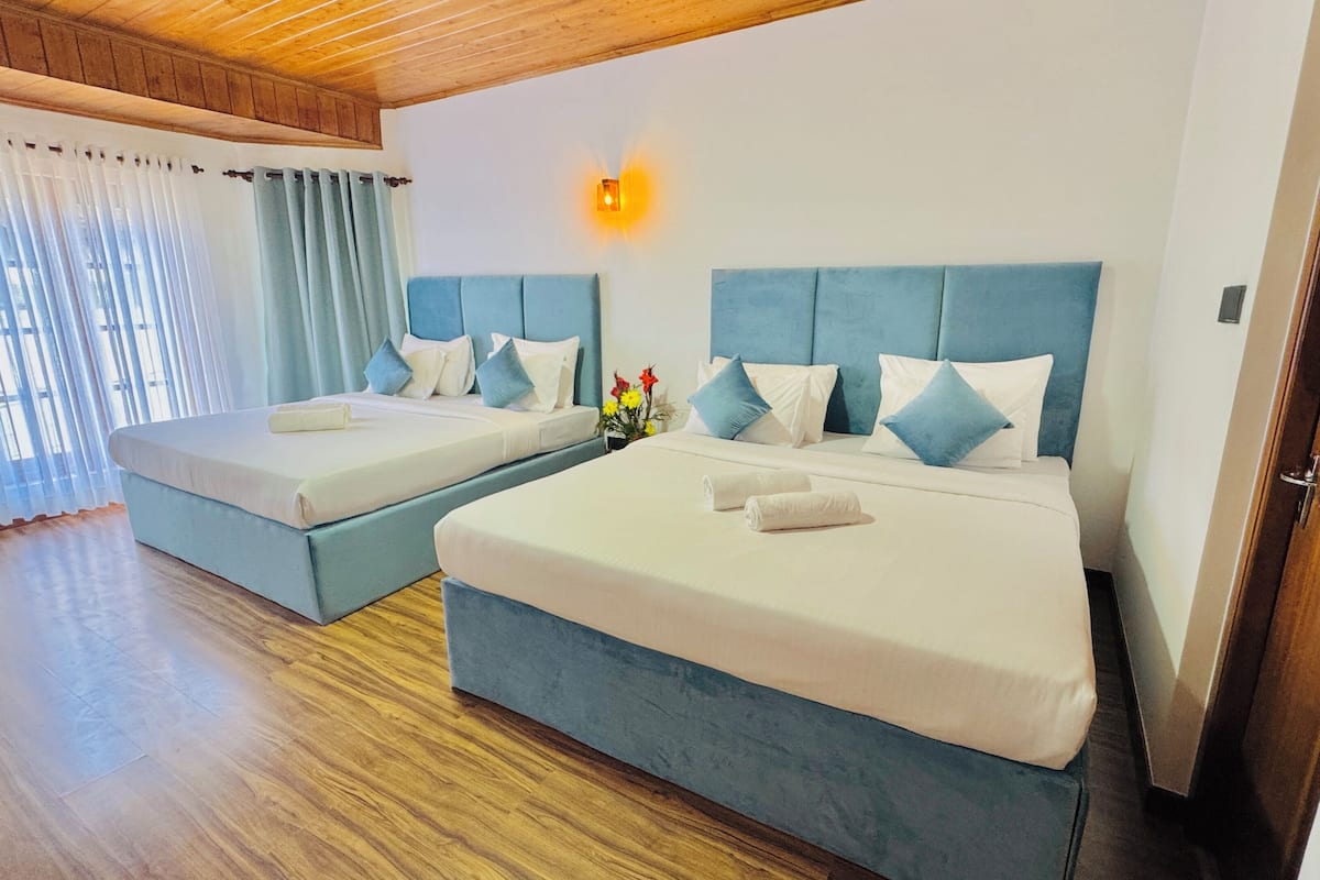 A hotel room with two beds, wooden flooring, a wooden ceiling, and a window with curtains.