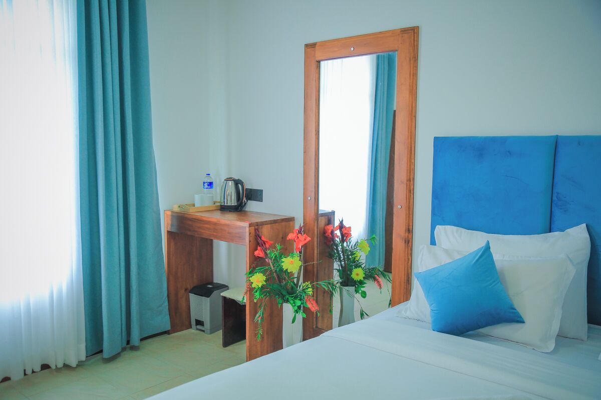 A hotel room with a bed, a wooden desk, a mirror, and a window with curtains.