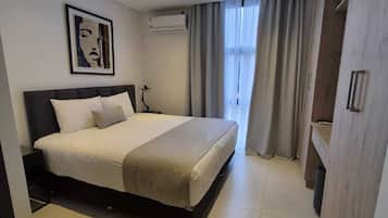 Habitación de hotel moderna con una cama grande, un televisor de pantalla plana y un baño con tocador de madera.