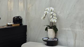 Una zona di accoglienza con parete in marmo, un cartello che riporta 'DIVINA TOWER', una scrivania reception nera, una panca bianca e un'orchidea in vaso.
