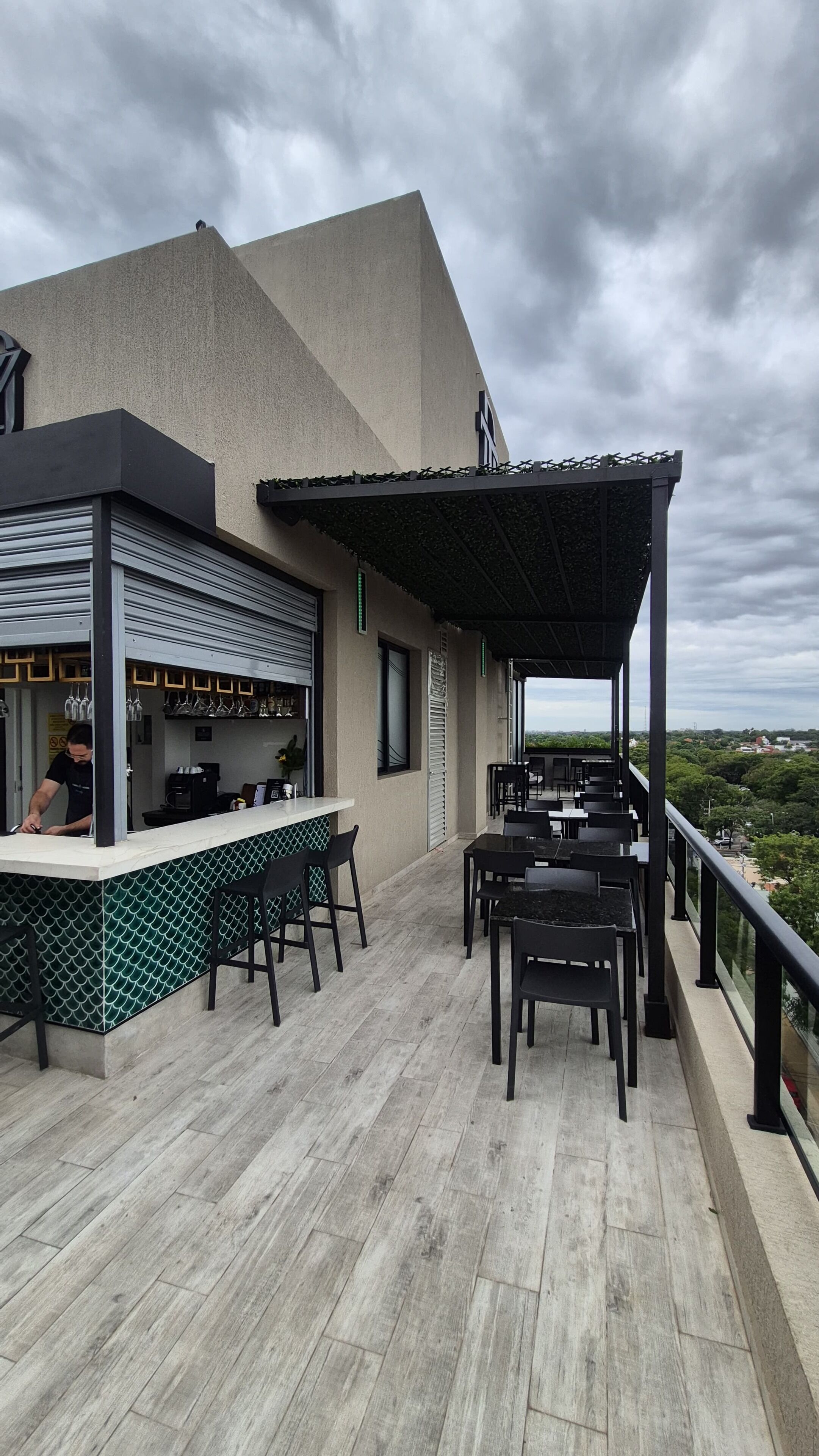 Una terraza exterior con zona de bar, asientos y vistas de la ciudad.