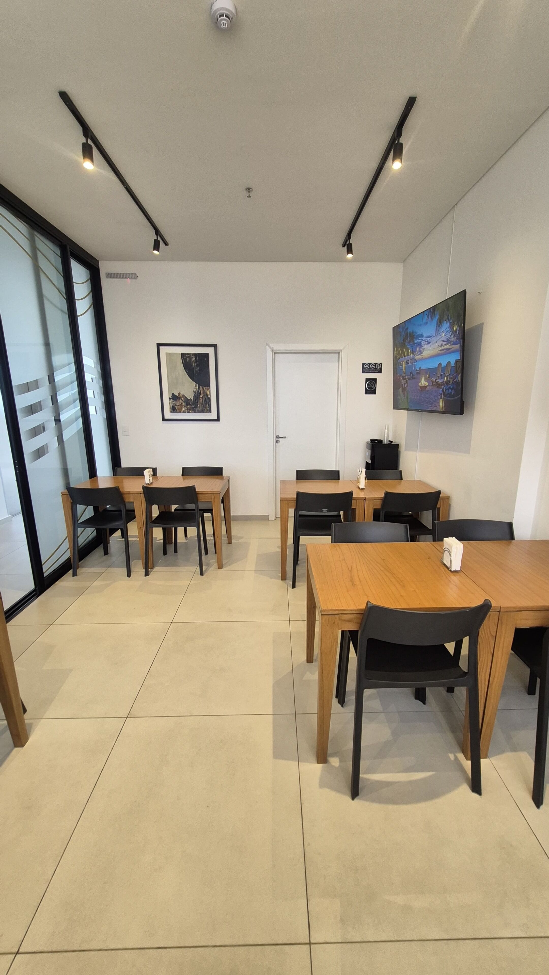 Un salón de conferencias con mesas y sillas, una puerta, un cuadro y una televisión montada.