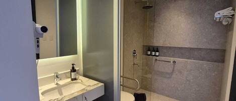 Un baño moderno con cabina de ducha de vidrio, tocador con encimera de mármol y un inodoro.