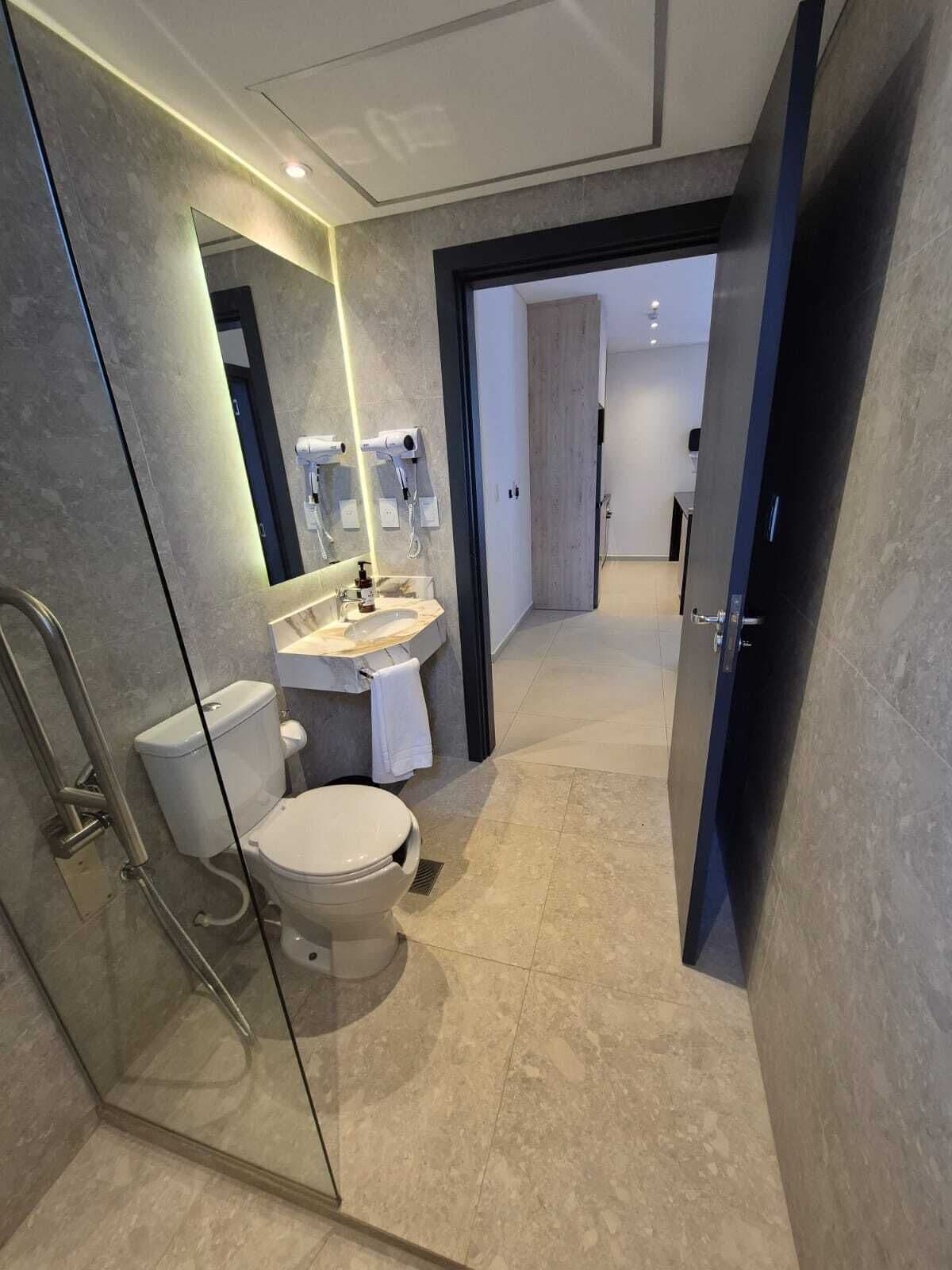 Un baño moderno con cabina de ducha de vidrio, inodoro, lavabo con espejo y una toalla colgada en la pared.