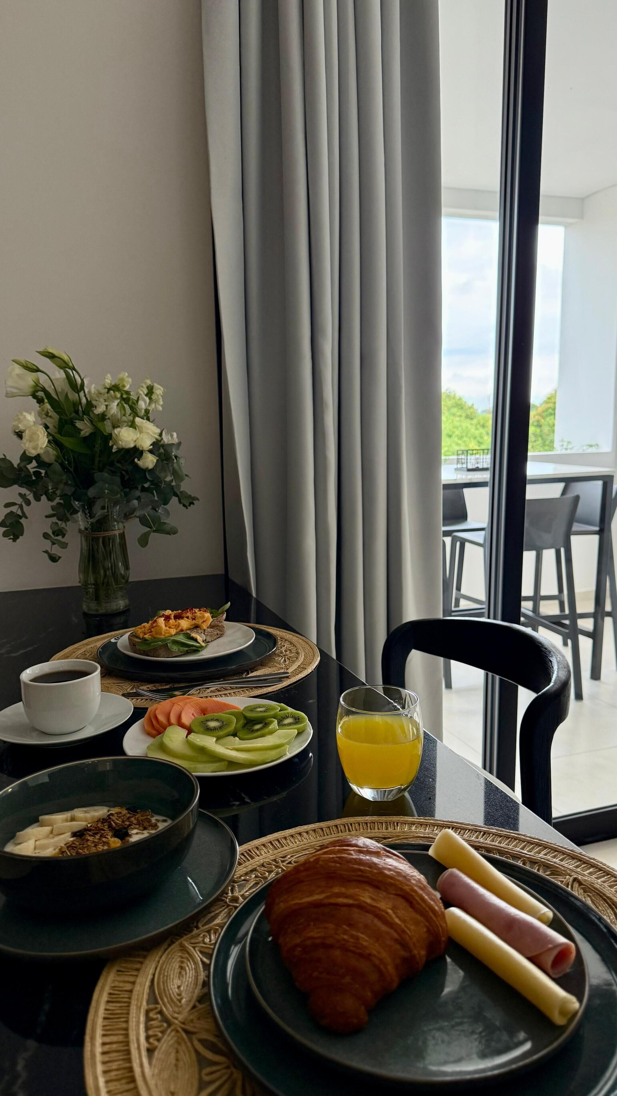Une table de petit-déjeuner avec des assiettes remplies de nourriture, un verre de jus d’orange et un croissant.