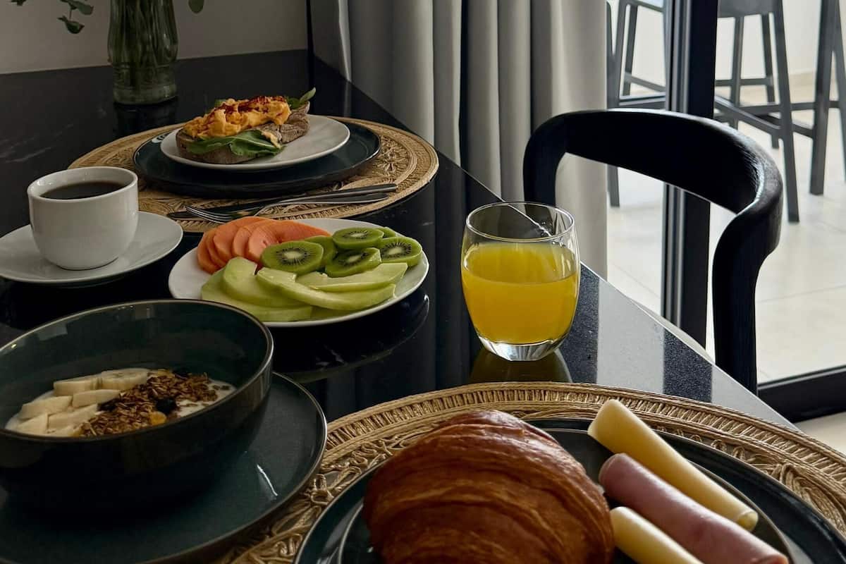 A breakfast table with plates of food, a glass of orange juice, and a croissant.