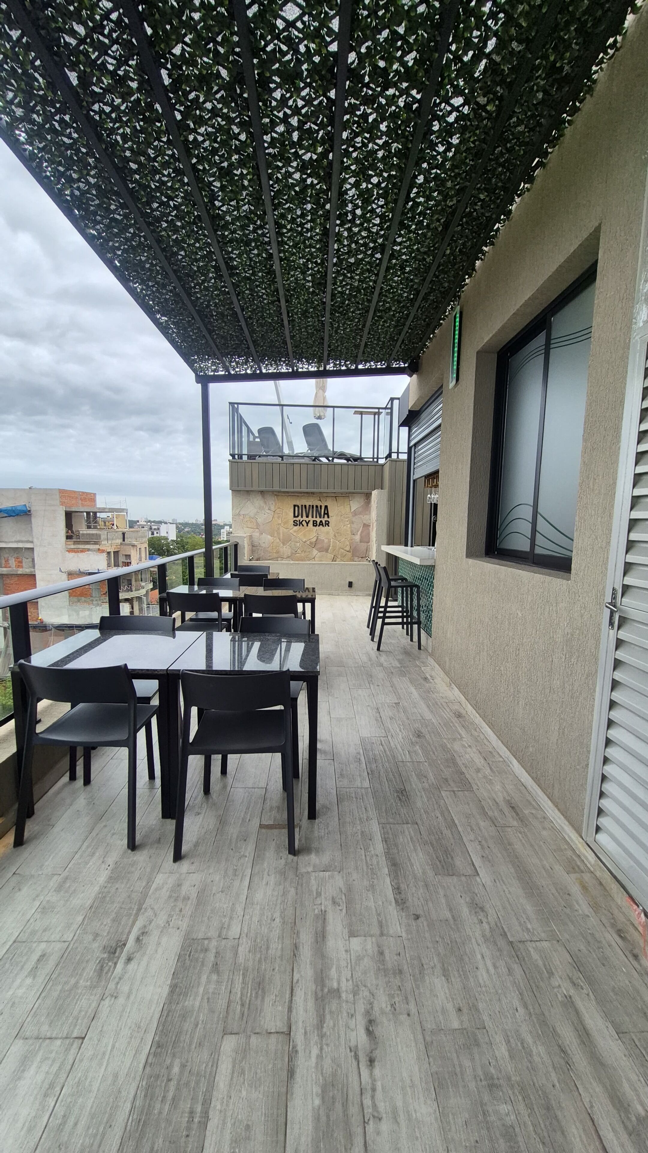 An outdoor patio with tables and chairs, a stone wall with 'DIVINA SKY BAR' signage, and a view of buildings in the background.