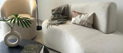 Una sala de estar moderna con un sofá curvo, una mesa de centro redonda, una lámpara de pie y un cuadro abstracto enmarcado.