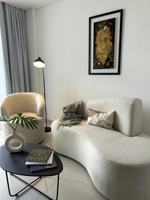 Un salon moderne avec un canapé aux lignes courbes, une table basse ronde, un lampadaire et un tableau abstrait encadré.