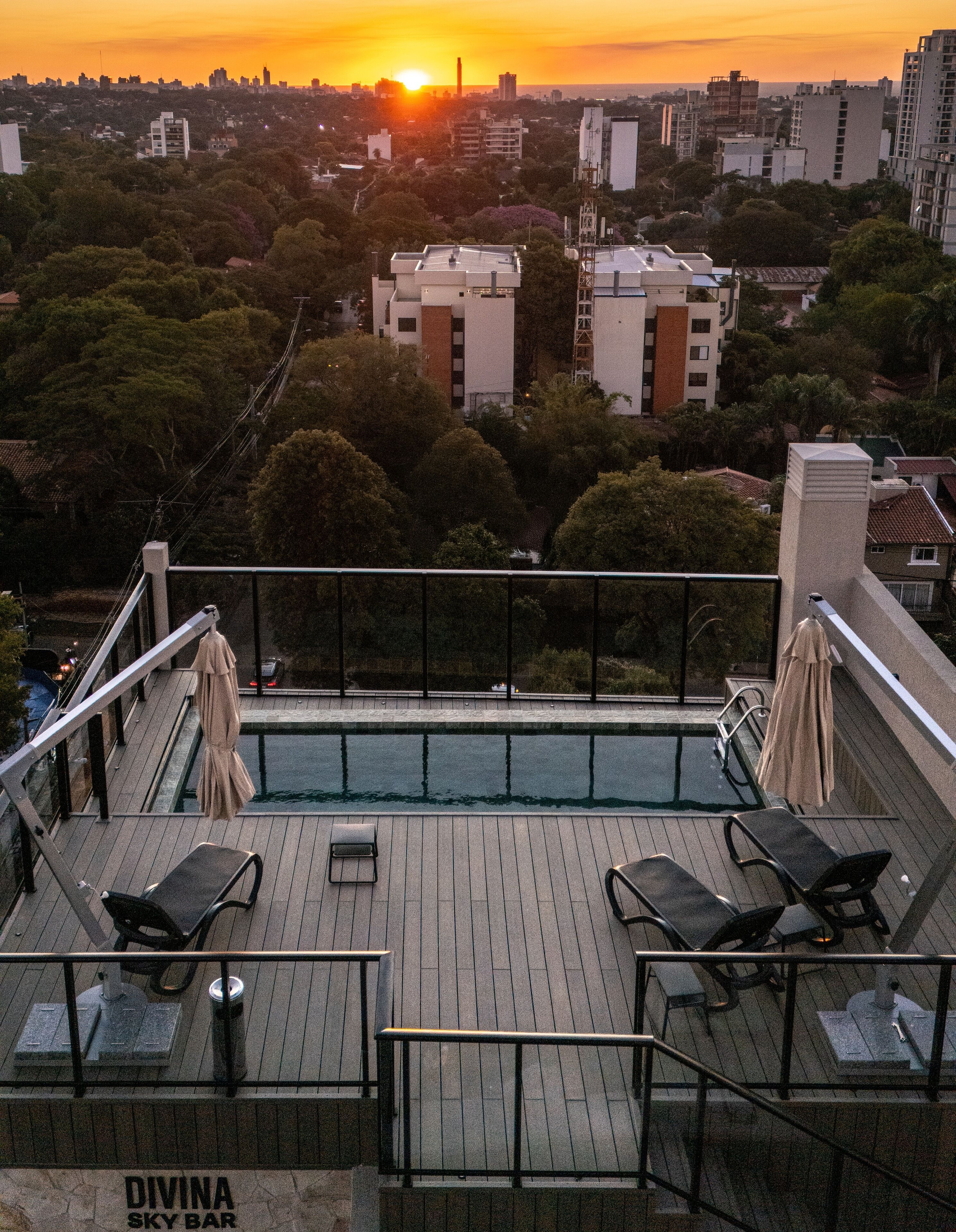 Una piscina en la azotea con sillones de descanso y vistas al horizonte urbano al atardecer.