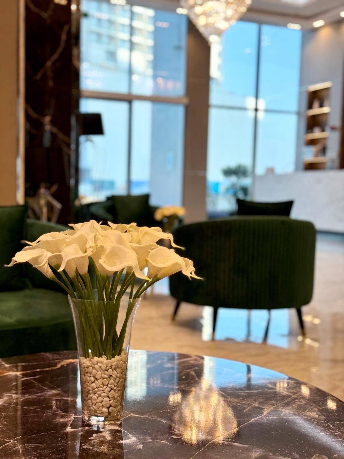 Een modern interieur met een marmeren tafel, een vaas witte bloemen en een groene bank.