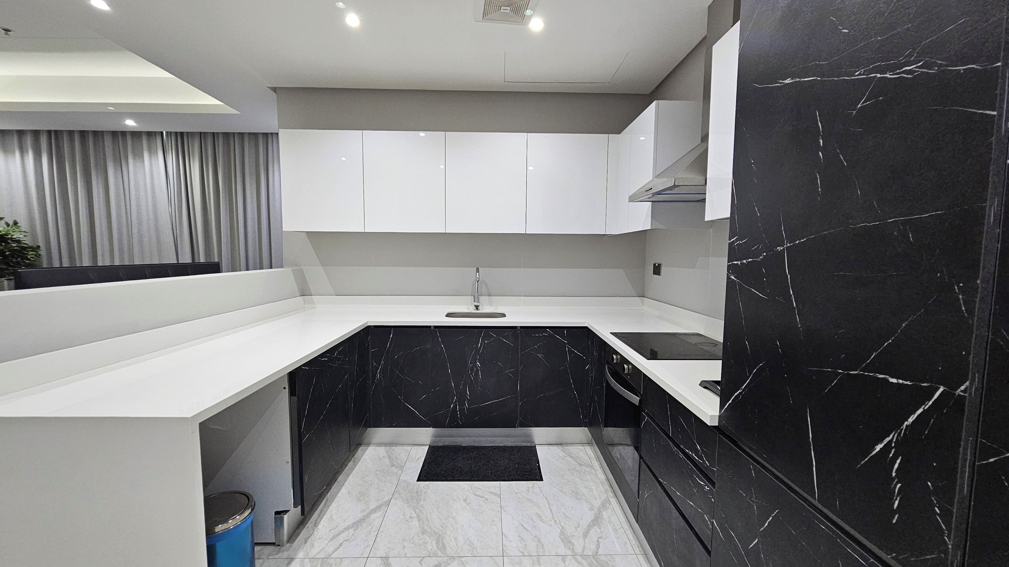 A modern kitchen with white cabinetry, black marble countertops, and a stainless steel sink.