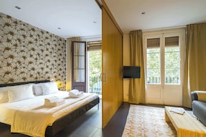 A hotel room with a bed, a desk, a chair, a TV, and a balcony with curtains. - Dana - stylish apartment moments from Plaza España (Barcelona)