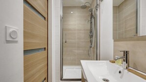 A modern bathroom with a glass-enclosed shower, a white sink, and wooden paneling. - 343 Michau - Cozy apartment near Sacré-Coeur (Paris 18 Buttes-Montmartre)