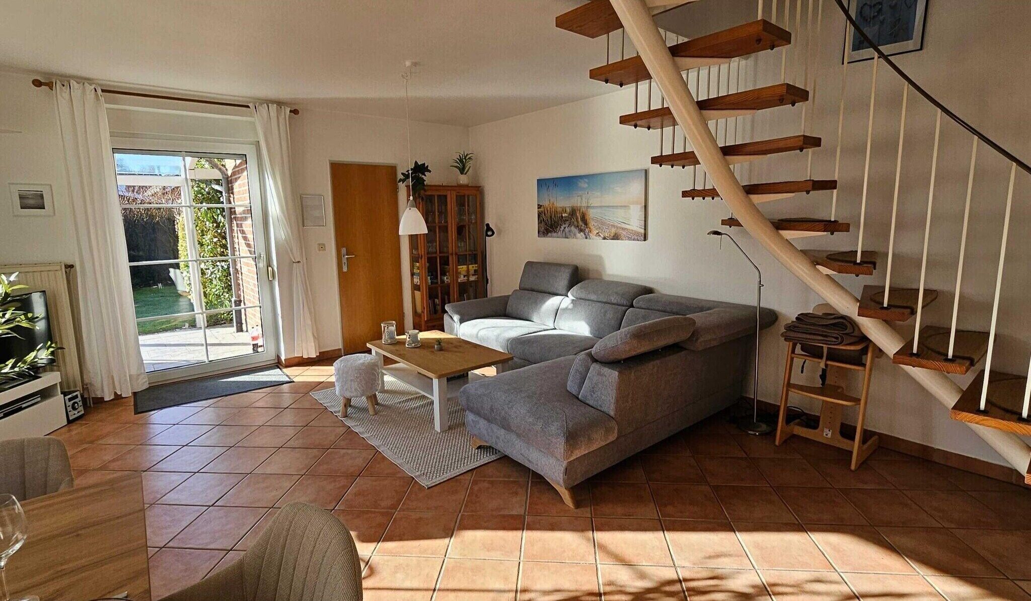 Ein Wohnzimmer mit einer Couch, einem Couchtisch, einem Fernseher, einer Treppe und einer zur Außenseite führenden Tür.