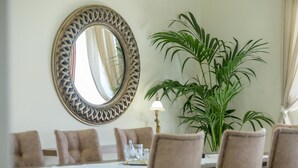 Un coin repas agrémenté d’un grand miroir rond, d’une table avec des chaises, d’une lampe et d’une grande plante en pot.