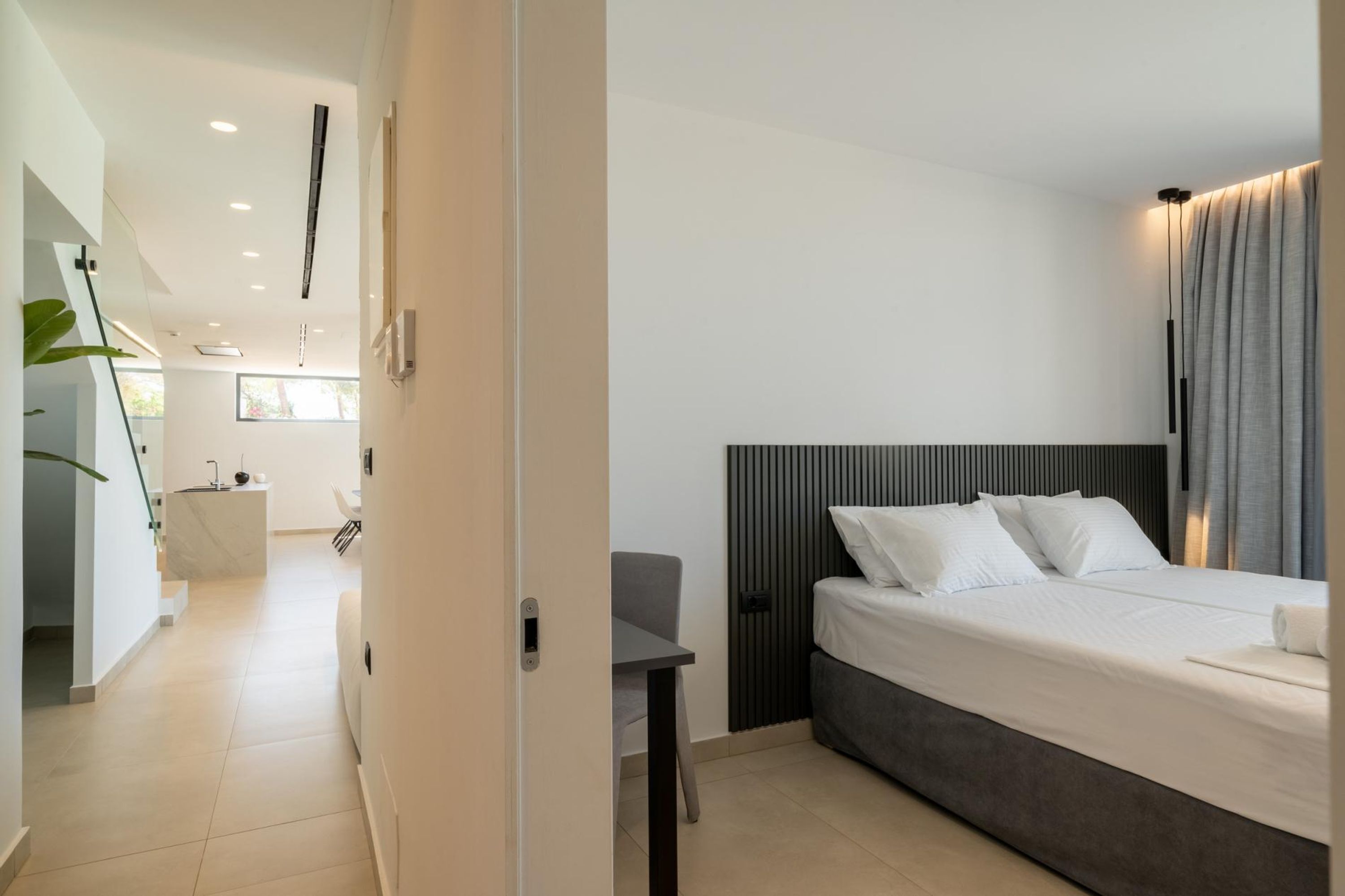 A modern hotel room with a large bed, a bedside table, and a view of the hallway.