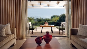 Un salon moderne avec un canapé, une table basse et deux vases. On aperçoit un coin repas avec une table et des chaises à travers une porte ouverte.